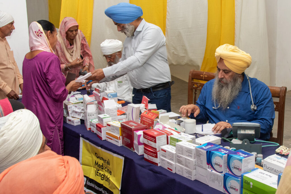2026-free-medical-camp-bakhshish-international-charitable-society-nussi-jalandhar-04 Physician consulting patients and prescribing medicine at Gurdwara Bakhshish Dham free medical camp 2026